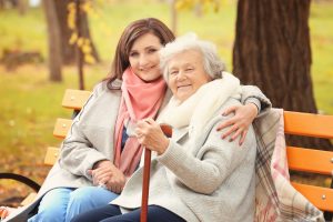 Senior,Woman,With,Cane,And,Young,Caregiver,Sitting,On,Bench